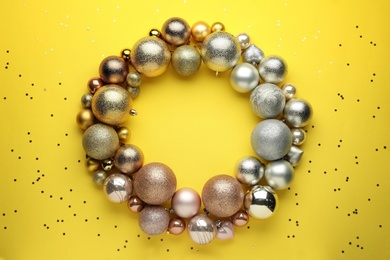 Bright festive wreath made of Christmas balls on yellow background, top view. Space for text Photo of Bright festive wreath made of Christmas balls on yellow background, top view. Space for text