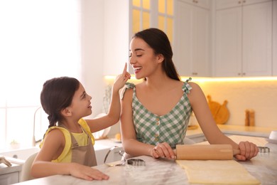 Mother with her cute little daughter having fun while rolling dough in kitchen Photo of Mother with her cute little daughter having fun while rolling dough in kitchen