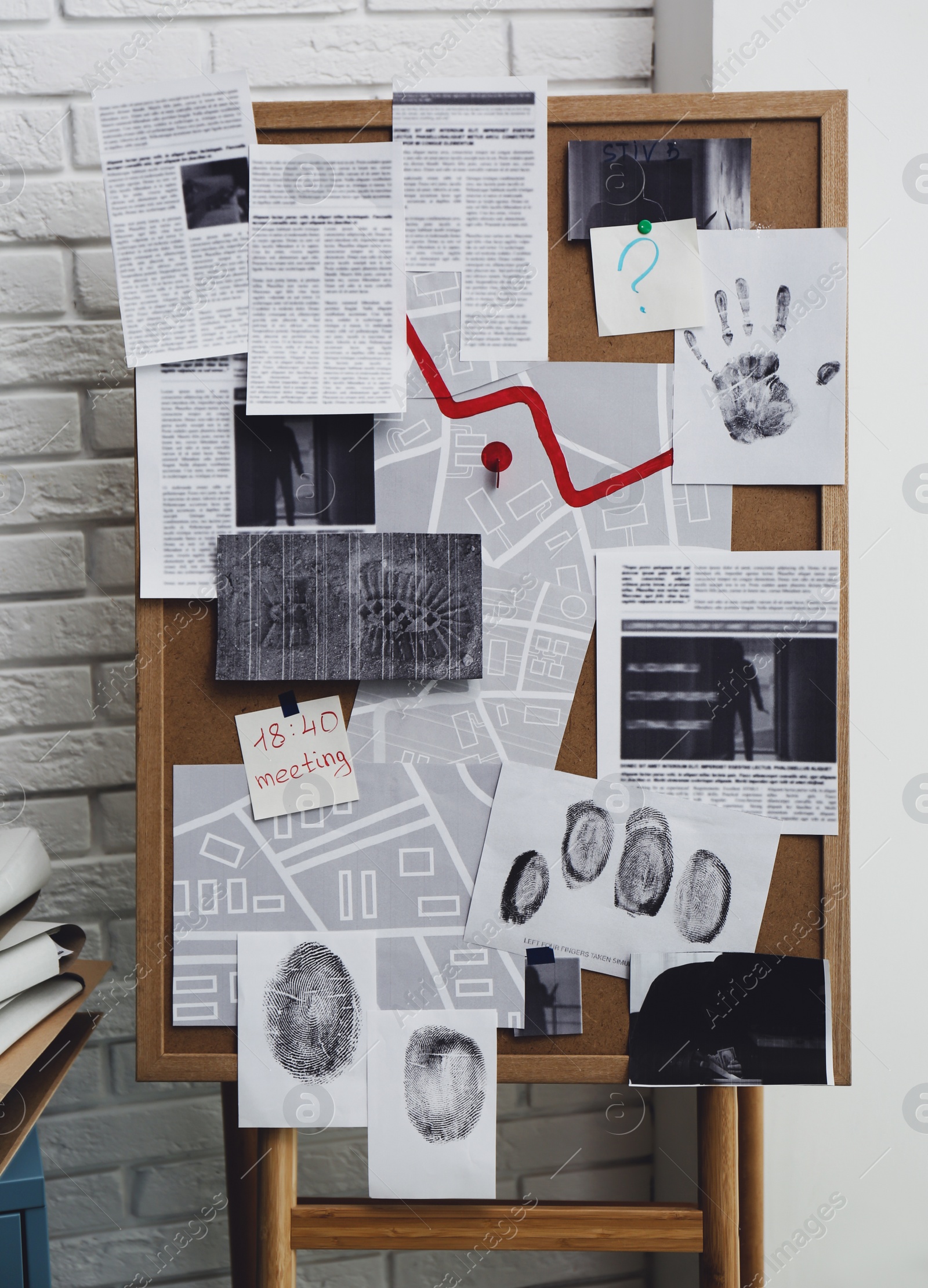 Detective board with fingerprints, crime scene photos and map near white brick wall indoors Photo of Detective board with fingerprints, crime scene photos and map near white brick wall indoors
