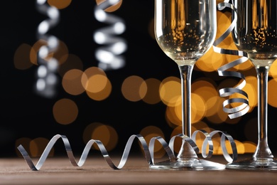 Glasses of champagne and serpentine streamers against black background with blurred lights, closeup. Space for text Photo of Glasses of champagne and serpentine streamers against black background with blurred lights, closeup. Space for text