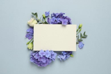 Beautiful composition with hortensia flowers and blank card on dusty light blue background, top view. Space for text Photo of Beautiful composition with hortensia flowers and blank card on dusty light blue background, top view. Space for text