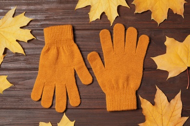 Stylish orange woolen gloves and dry leaves on wooden table, flat lay Photo of Stylish orange woolen gloves and dry leaves on wooden table, flat lay