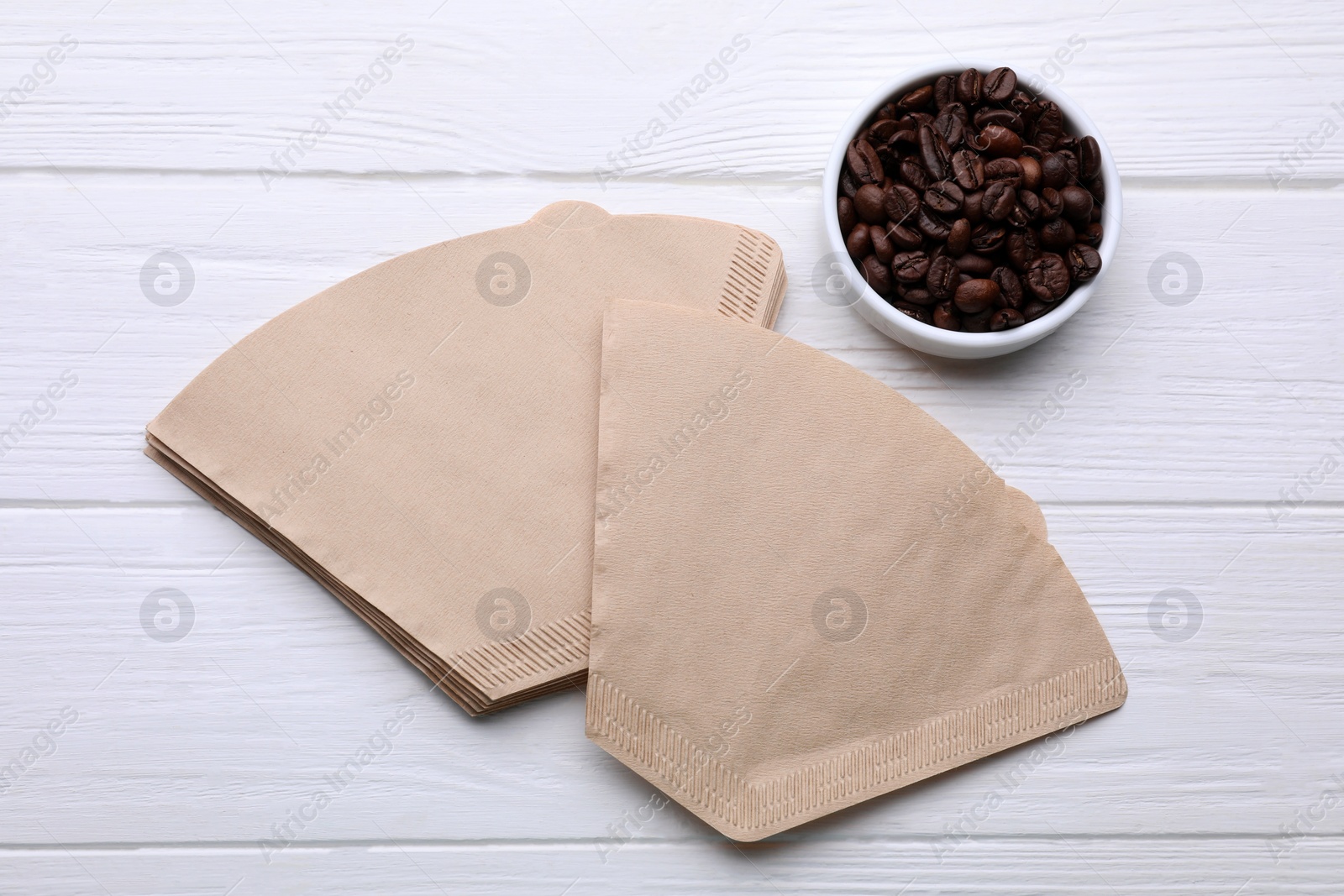 Paper coffee filters and beans on white wooden table, flat lay Photo of Paper coffee filters and beans on white wooden table, flat lay