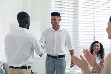 Boss shaking hand with new employee and coworkers applauding in office Photo of Boss shaking hand with new employee and coworkers applauding in office