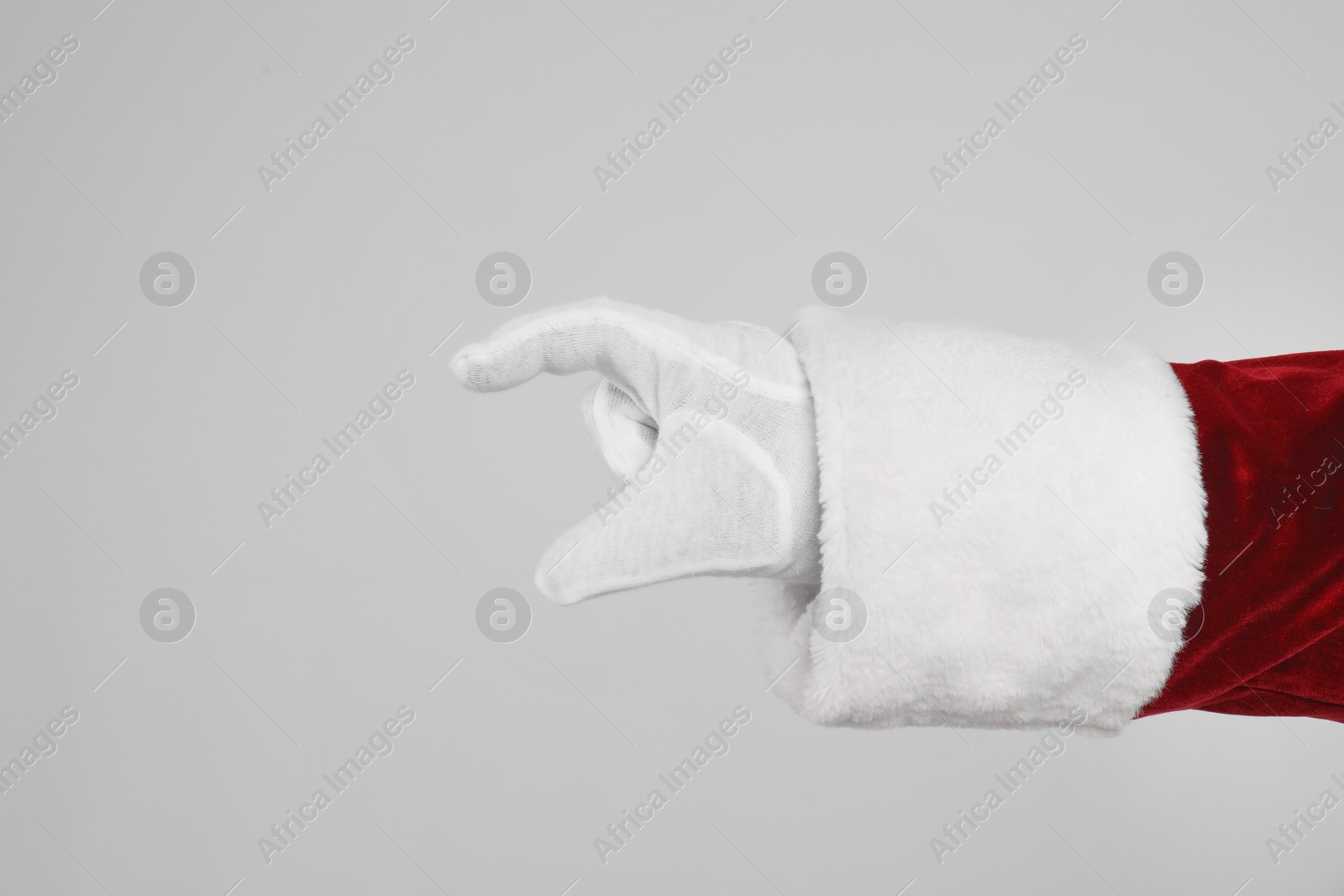 Santa Claus holding something on light grey background, closeup of hand Photo of Santa Claus holding something on light grey background, closeup of hand
