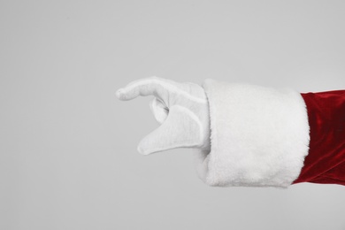 Santa Claus holding something on light grey background, closeup of hand Photo of Santa Claus holding something on light grey background, closeup of hand