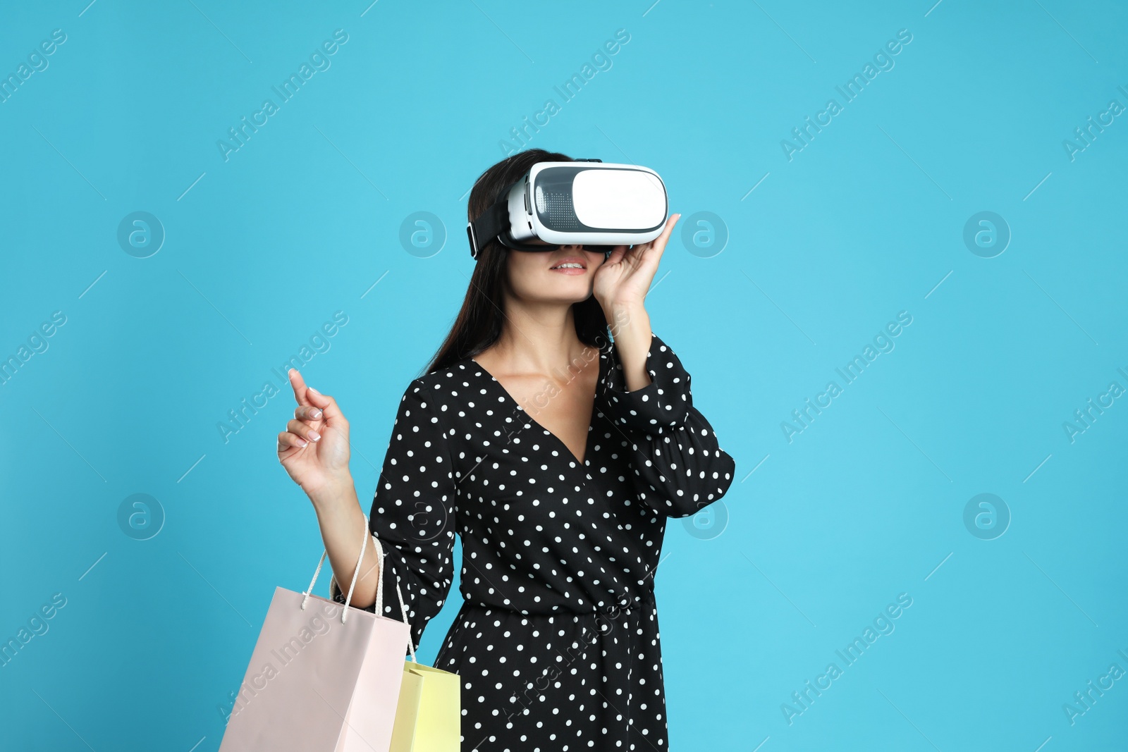 Woman with shopping bags using virtual reality headset on light blue background Photo of Woman with shopping bags using virtual reality headset on light blue background