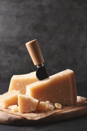 Delicious parmesan cheese with knife on black table Photo of Delicious parmesan cheese with knife on black table