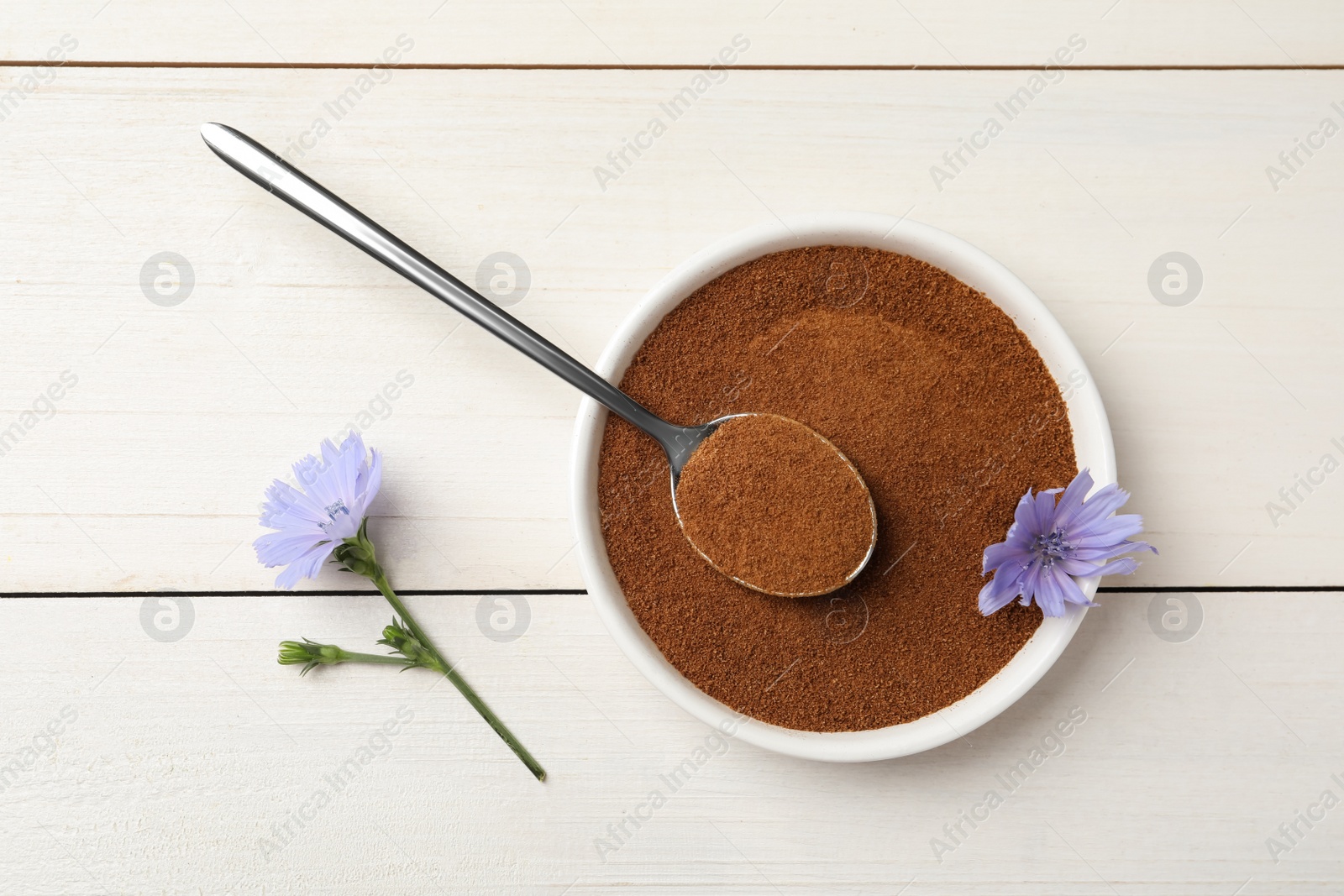 Bowl of chicory powder and flowers on white wooden table, flat lay Photo of Bowl of chicory powder and flowers on white wooden table, flat lay