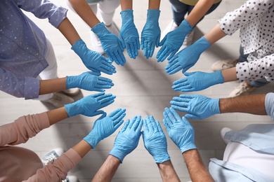 People in blue medical gloves joining hands indoors, top view Photo of People in blue medical gloves joining hands indoors, top view