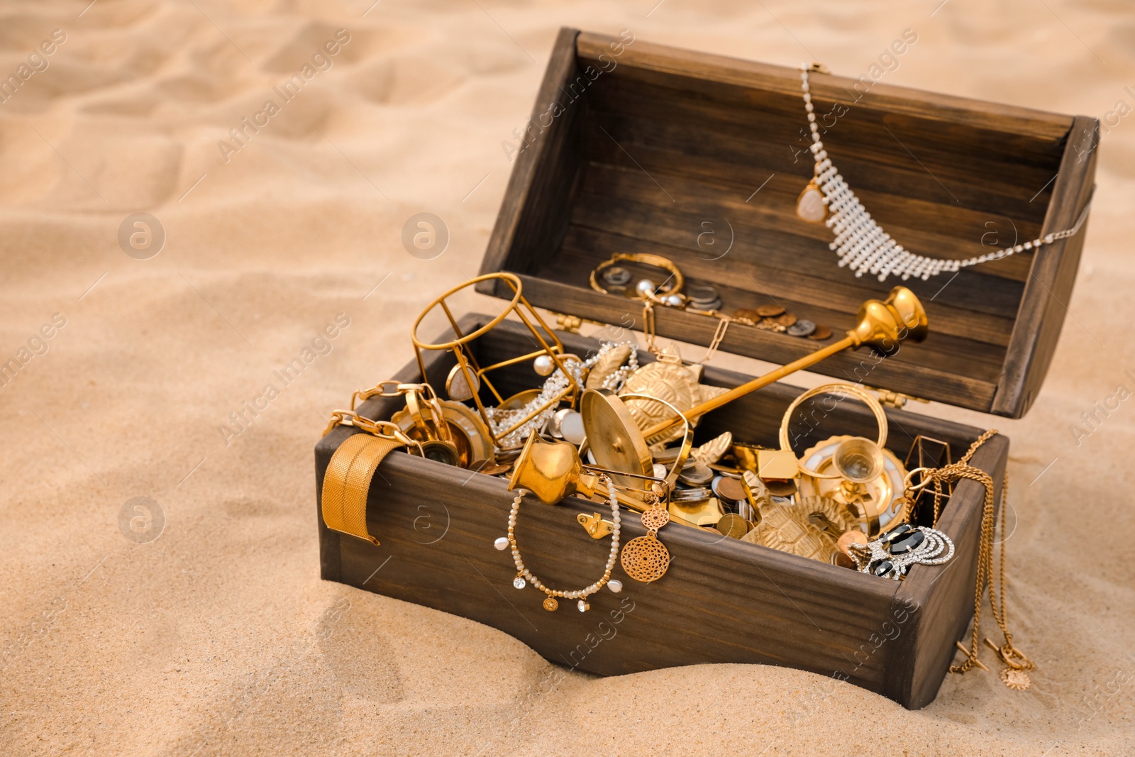 Open wooden chest with treasures on sand Photo of Open wooden chest with treasures on sand