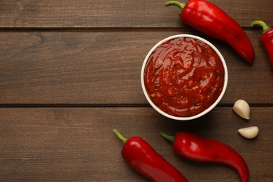 Delicious adjika sauce in bowl and ingredients on wooden table, flat lay. Space for text Photo of Delicious adjika sauce in bowl and ingredients on wooden table, flat lay. Space for text