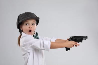 Cute little detective with revolver on grey background Photo of Cute little detective with revolver on grey background