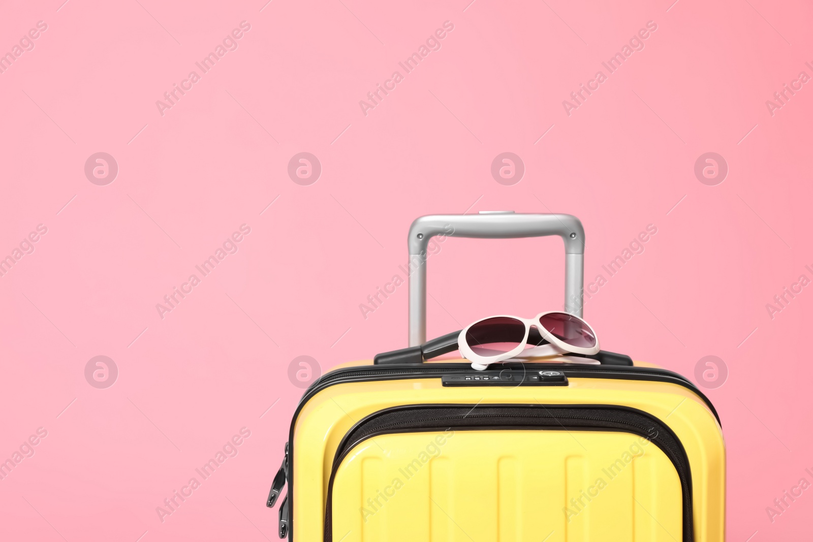 Photo of Yellow suitcase with sunglasses on pink background. Space for text