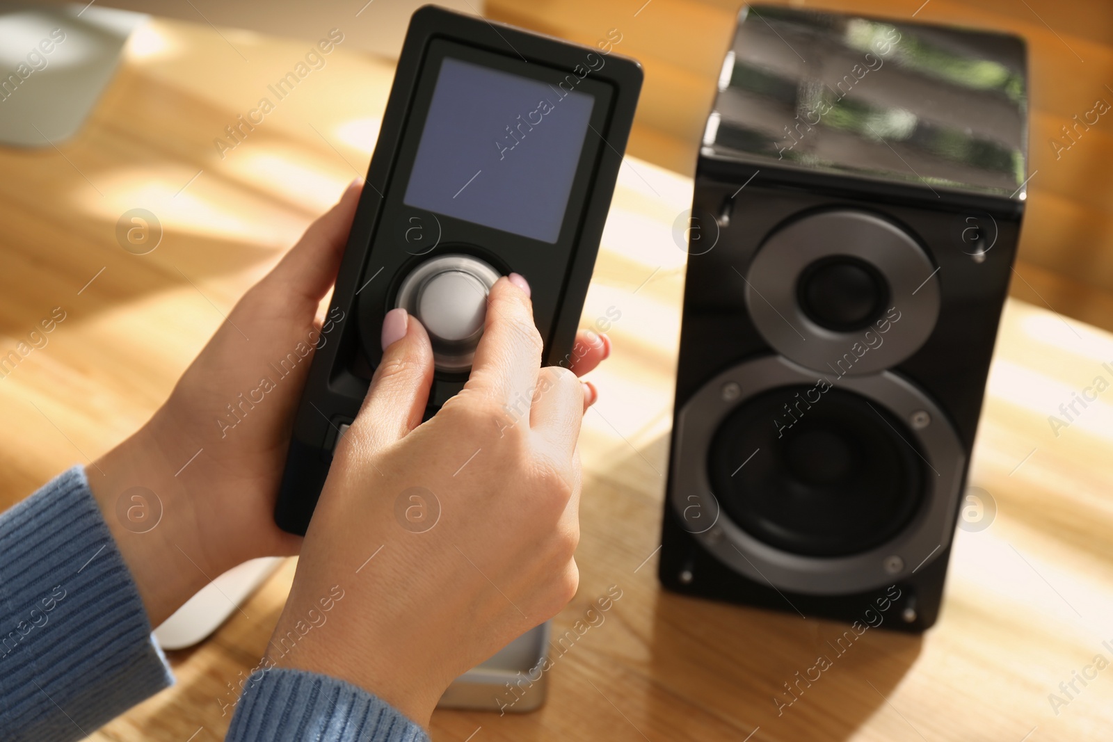 Woman using remote to control audio speakers at wooden table indoors, closeup Photo of Woman using remote to control audio speakers at wooden table indoors, closeup