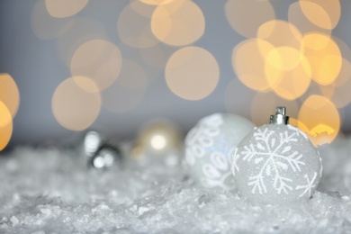 Beautiful white Christmas balls on snow against blurred festive lights, space for text Photo of Beautiful white Christmas balls on snow against blurred festive lights, space for text