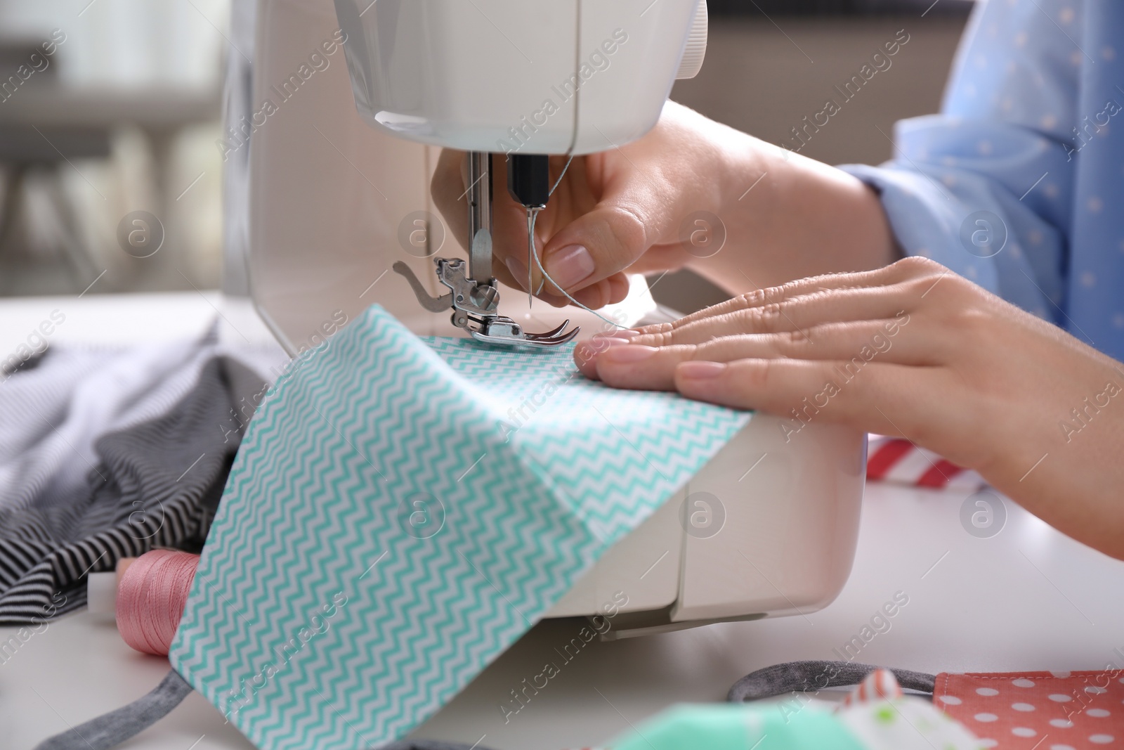 Woman making cloth mask with sewing machine at white table, closeup Photo of Woman making cloth mask with sewing machine at white table, closeup