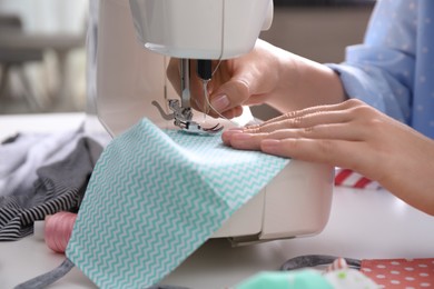 Photo of Woman making cloth mask with sewing machine at white table, closeup