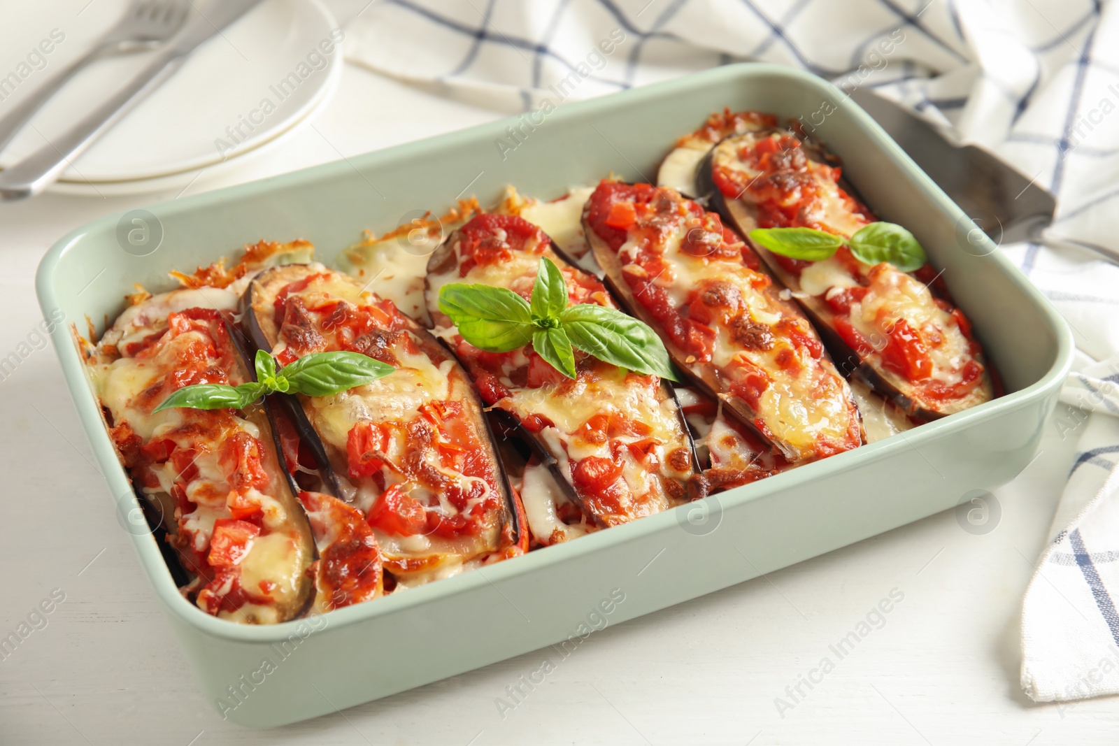 Baked eggplant with tomatoes, cheese and basil in dishware on white wooden table Photo of Baked eggplant with tomatoes, cheese and basil in dishware on white wooden table