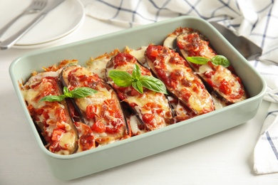 Baked eggplant with tomatoes, cheese and basil in dishware on white wooden table Photo of Baked eggplant with tomatoes, cheese and basil in dishware on white wooden table