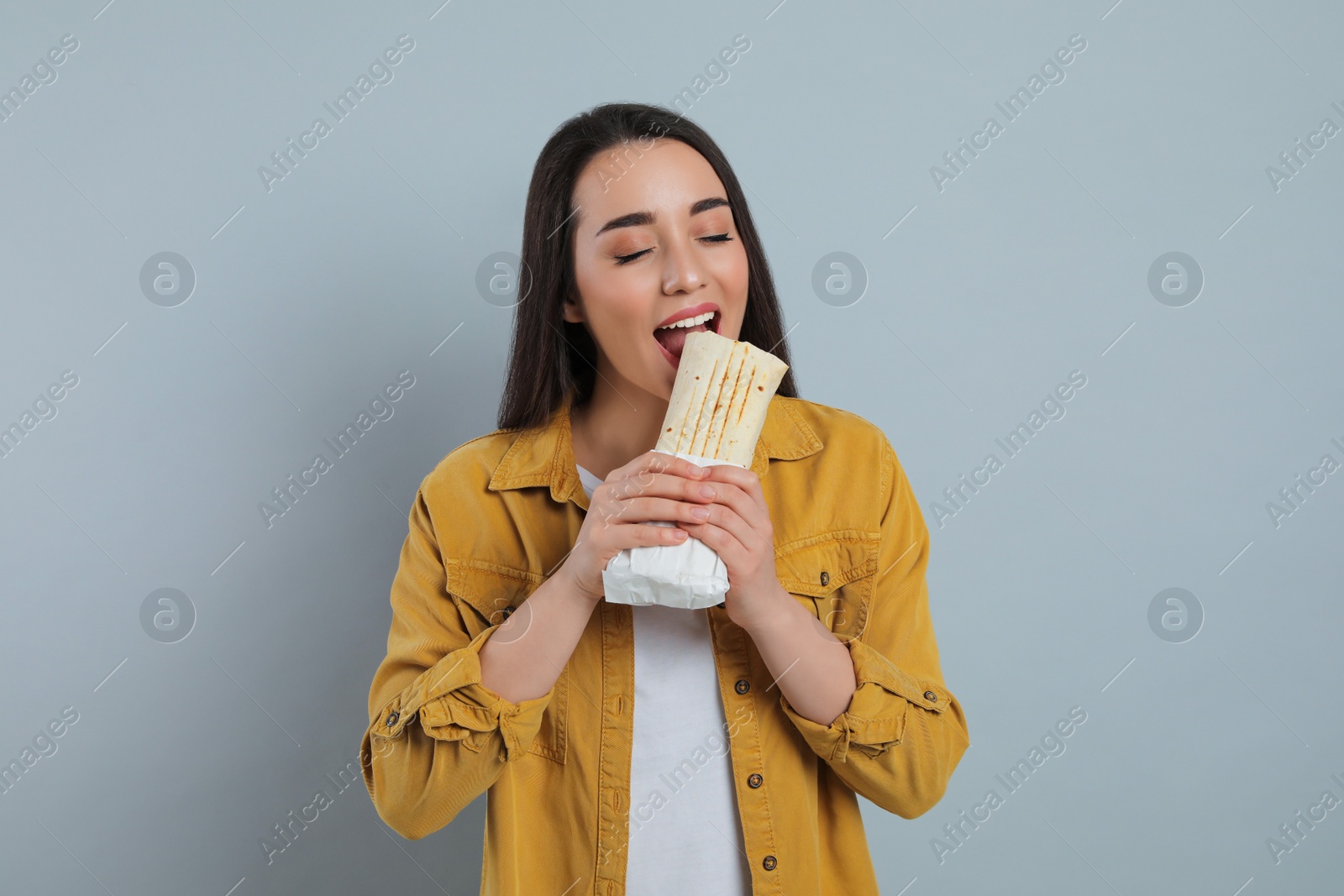 Young woman eating tasty shawarma on grey background Photo of Young woman eating tasty shawarma on grey background