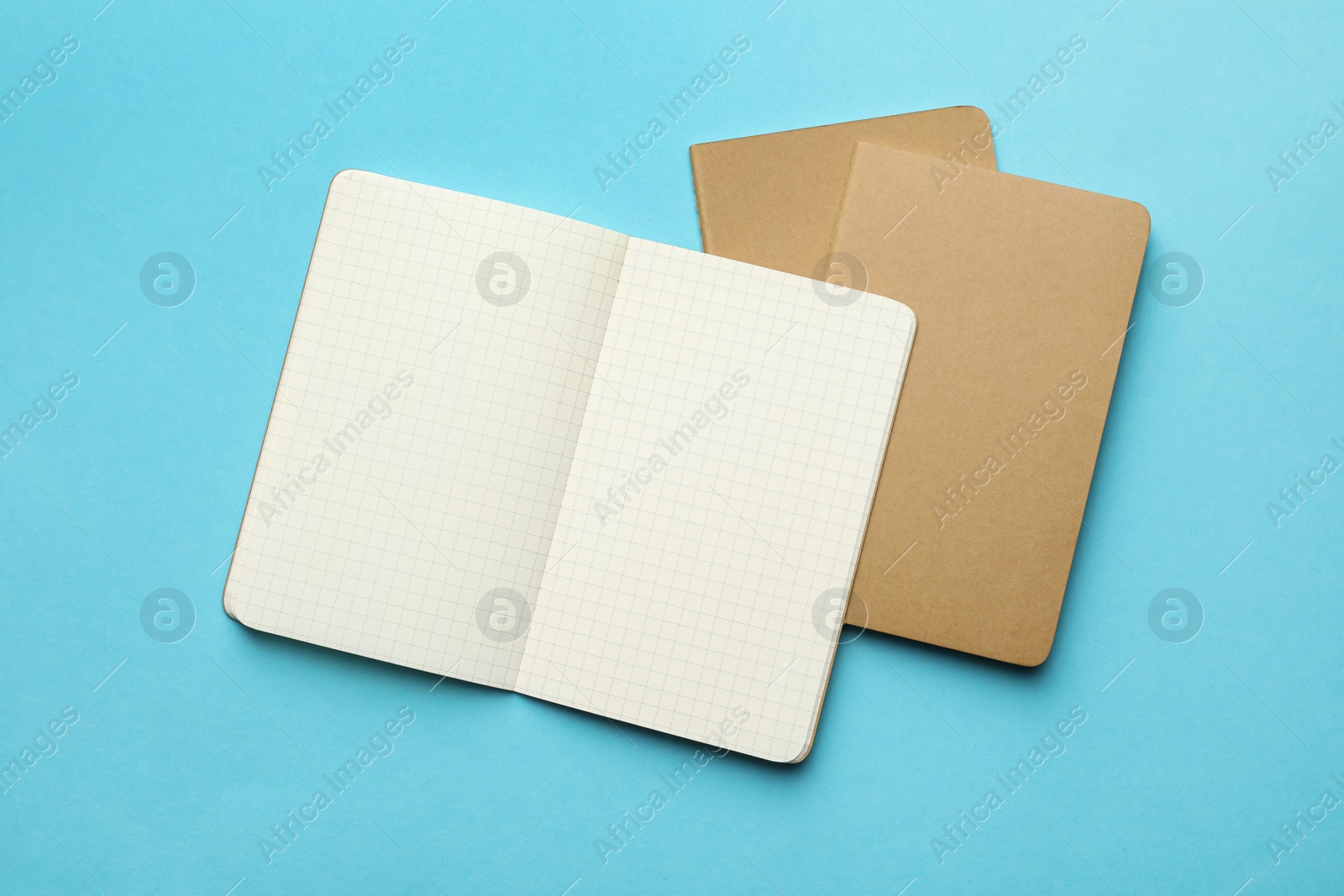 Stylish kraft notebooks on light blue background, flat lay Photo of Stylish kraft notebooks on light blue background, flat lay
