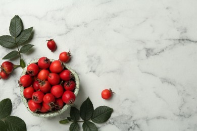 Ripe rose hip berries with green leaves on white marble table, flat lay. Space for text Photo of Ripe rose hip berries with green leaves on white marble table, flat lay. Space for text