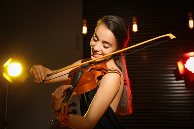 Beautiful young woman playing violin in dark room Photo of Beautiful young woman playing violin in dark room