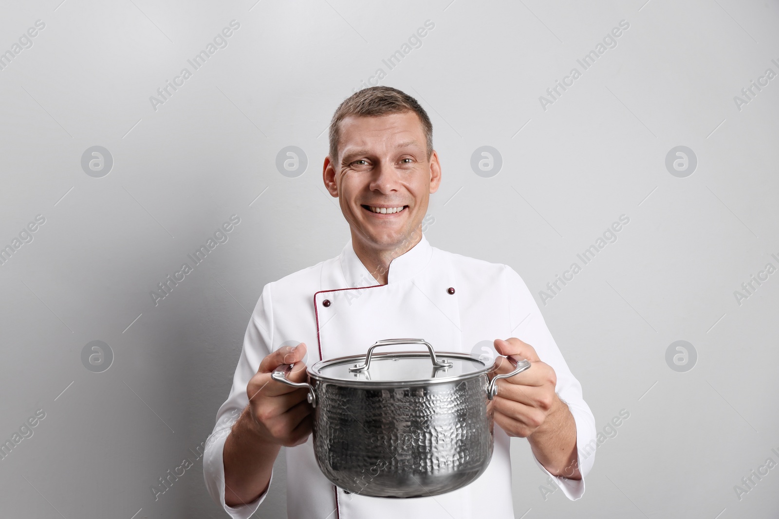Happy male chef with cooking pot on light grey background Photo of Happy male chef with cooking pot on light grey background