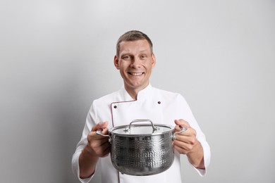 Happy male chef with cooking pot on light grey background Photo of Happy male chef with cooking pot on light grey background