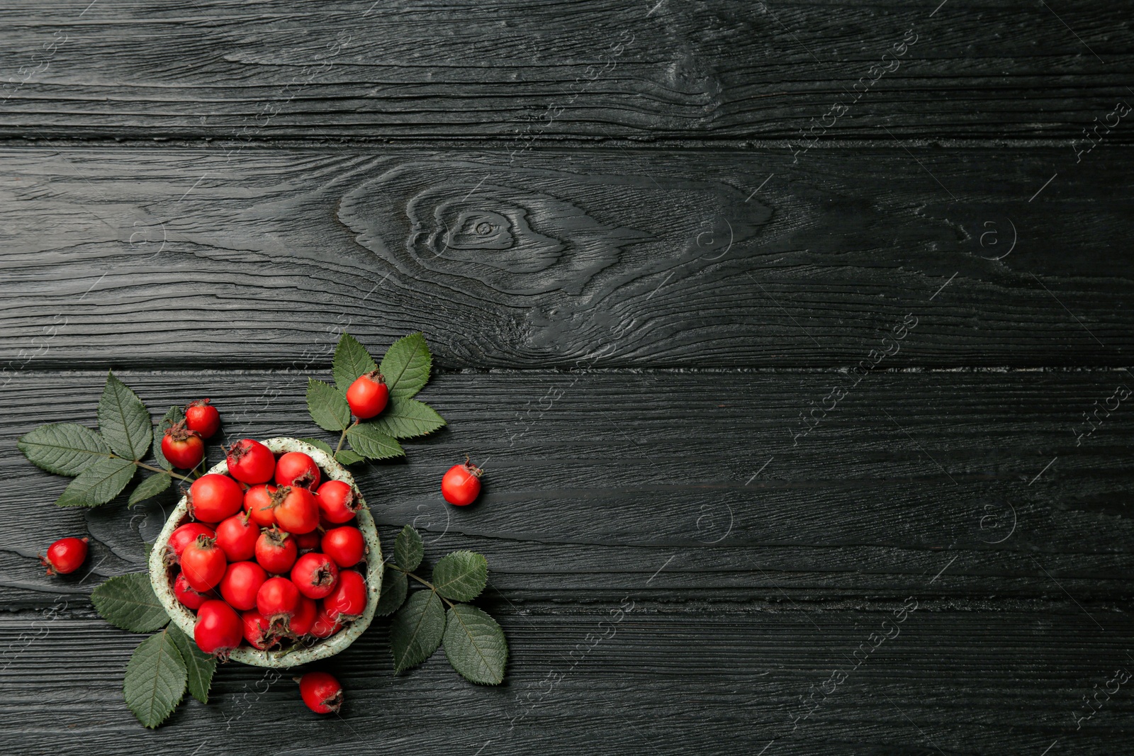 Ripe rose hip berries with green leaves on black wooden table, flat lay. Space for text Photo of Ripe rose hip berries with green leaves on black wooden table, flat lay. Space for text