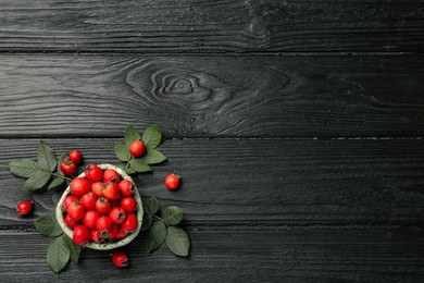 Ripe rose hip berries with green leaves on black wooden table, flat lay. Space for text Photo of Ripe rose hip berries with green leaves on black wooden table, flat lay. Space for text
