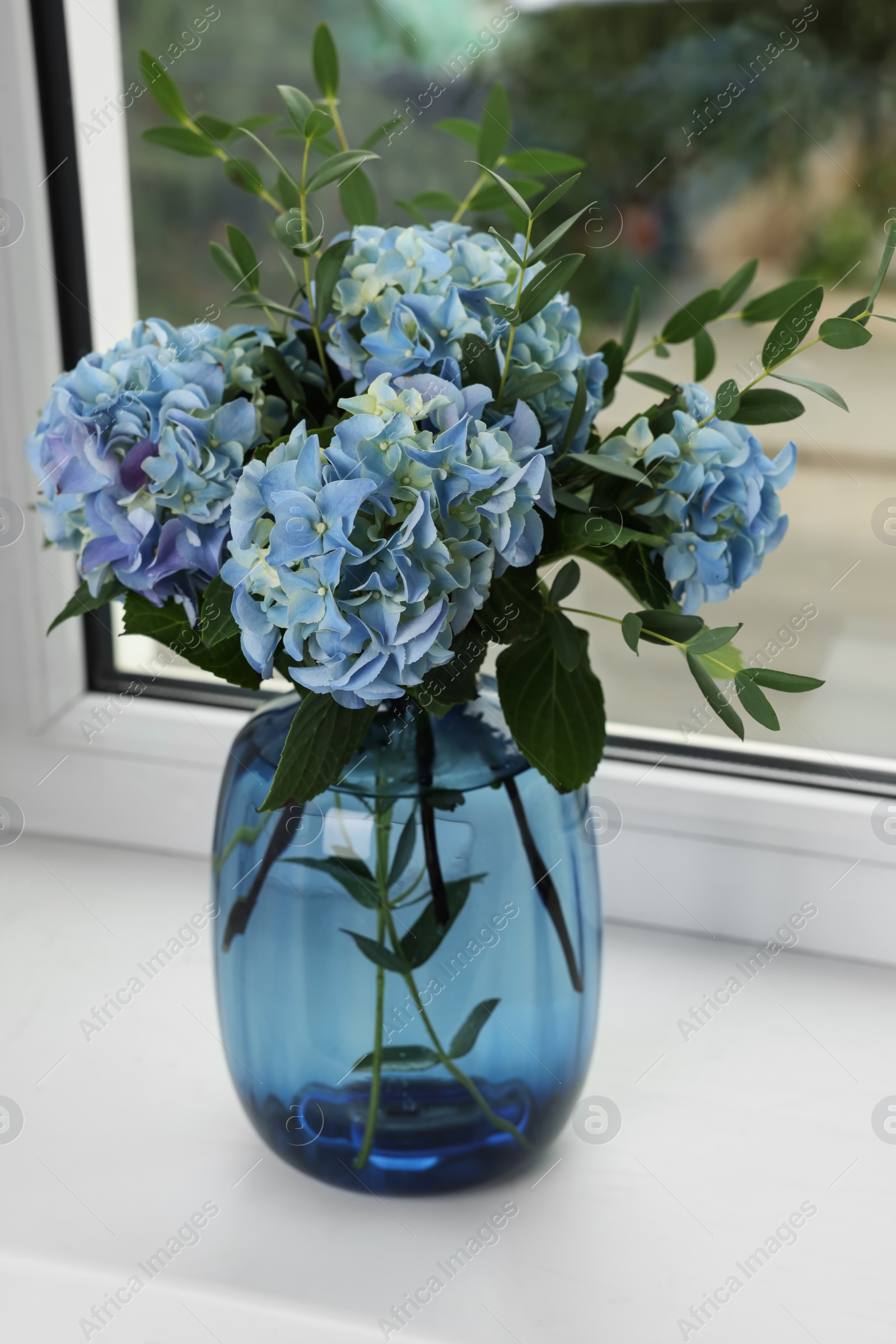 Beautiful blue hortensia flowers in vase on window sill indoors Photo of Beautiful blue hortensia flowers in vase on window sill indoors