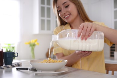 Young woman pouring milk from gallon bottle into plate with breakfast cereal at white marble table in kitchen Photo of Young woman pouring milk from gallon bottle into plate with breakfast cereal at white marble table in kitchen