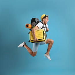 Photo of Emotional male tourist with travel backpack and suitcase jumping on turquoise background