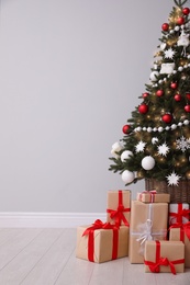Christmas tree and gift boxes near light grey wall, space for text Photo of Christmas tree and gift boxes near light grey wall, space for text