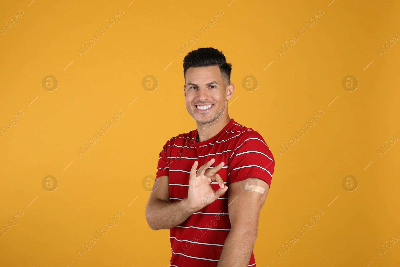 Vaccinated man with medical plaster on his arm showing okay gesture against yellow background Photo of Vaccinated man with medical plaster on his arm showing okay gesture against yellow background