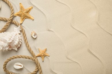 Photo of Beautiful sea stars, shells and rope on sand, flat lay. Space for text