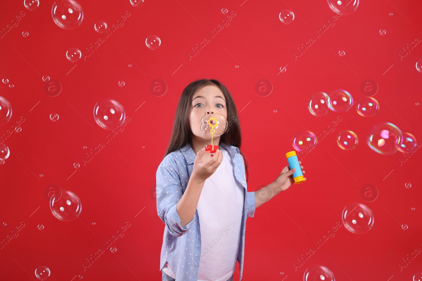 Photo of Little girl blowing soap bubbles on red background