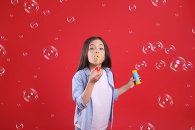 Little girl blowing soap bubbles on red background Photo of Little girl blowing soap bubbles on red background