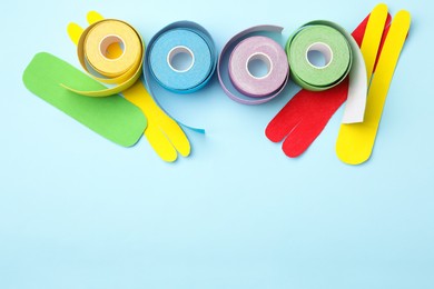 Bright kinesio tape rolls and pieces on light blue background, flat lay. Space for text Photo of Bright kinesio tape rolls and pieces on light blue background, flat lay. Space for text