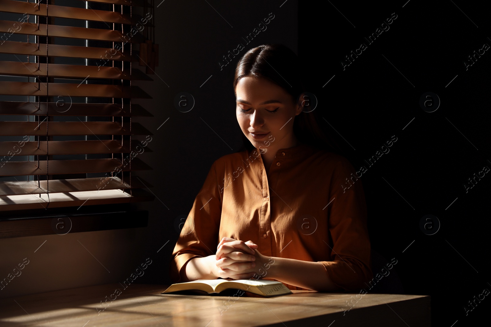 Religious young woman praying over Bible at wooden table indoors Photo of Religious young woman praying over Bible at wooden table indoors