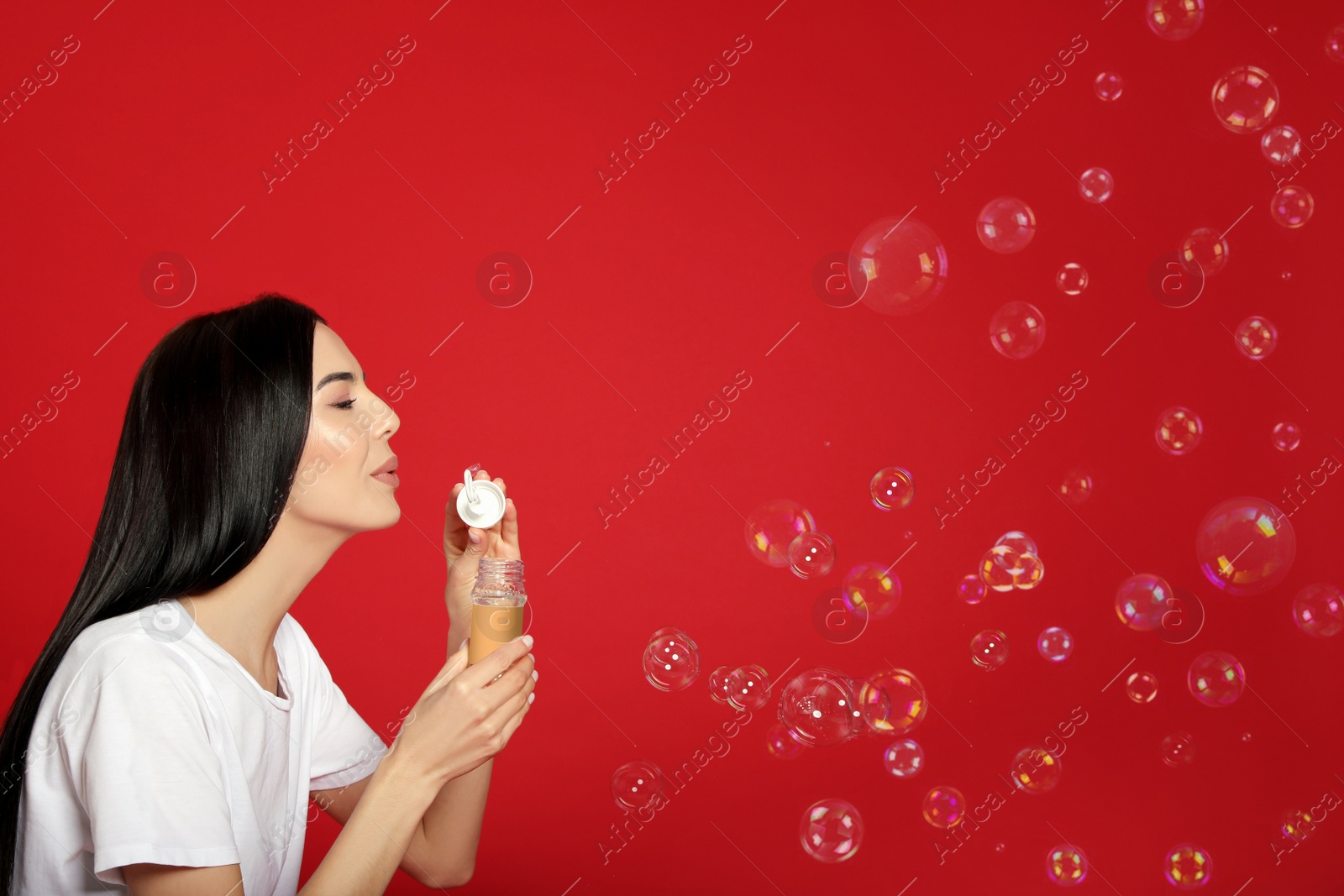 Young woman blowing soap bubbles on red background, space for text Photo of Young woman blowing soap bubbles on red background, space for text
