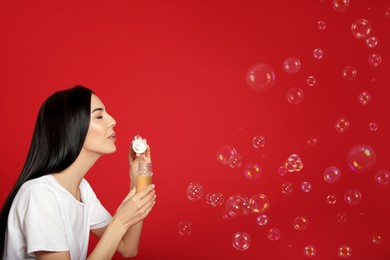 Young woman blowing soap bubbles on red background, space for text Photo of Young woman blowing soap bubbles on red background, space for text