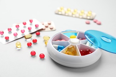 Plastic box with different pills on light grey background Photo of Plastic box with different pills on light grey background